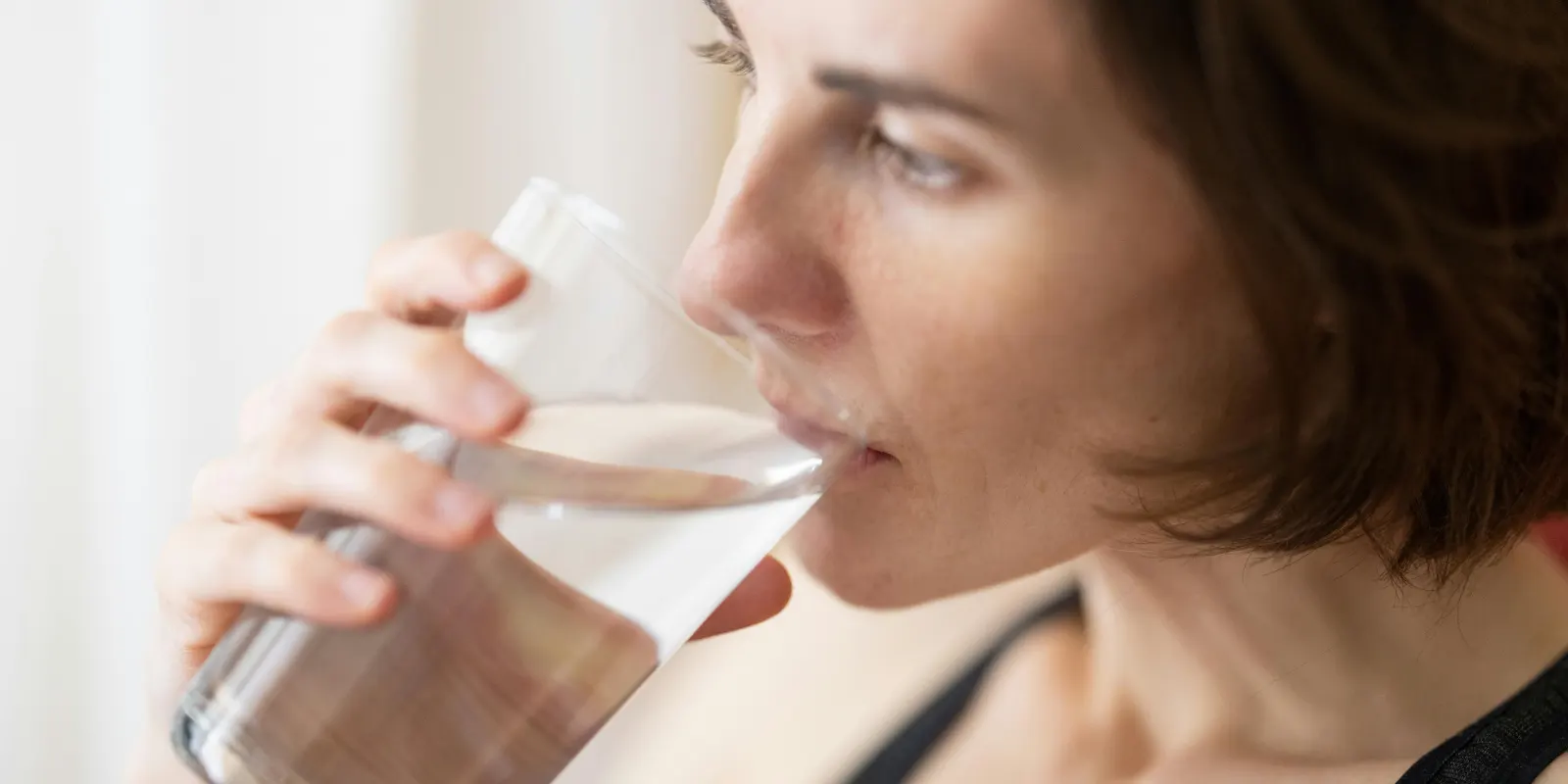 Woman enjoys a glass of water treated by a water softener, preventing limescale without removing natural minerals